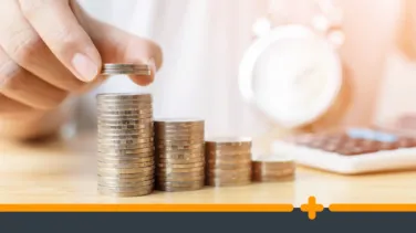 Ręka układająca monety w rosnące stosy na stole na tle zegarka i kalkulatora