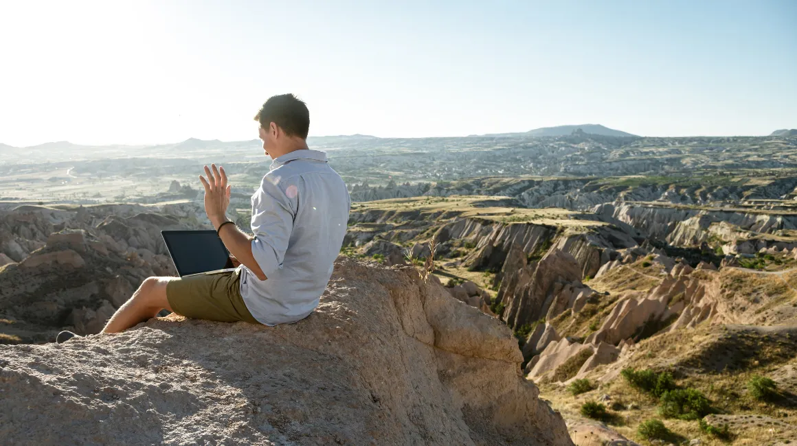 Mężczyzna pracujący z laptopem na szczycie skały z widokiem na malowniczy krajobraz